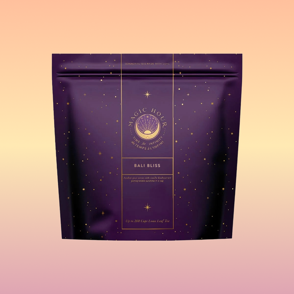 A purple and gold resealable pouch labeled "Magic Hour Bali Bliss" features celestial graphics on a pastel background, highlighting the Coconut-Lime &amp; Ginger-Melon White Tea loose leaf blend.