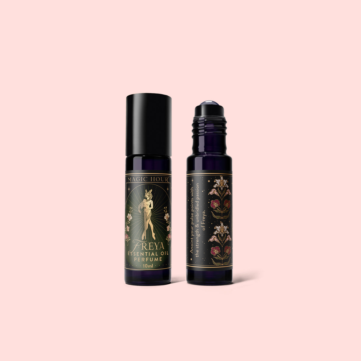 Two dark glass roller bottles with vintage floral labels stand upright on a pale pink background; one is labeled “Freya’s Essential Oil Perfume,” capturing the mystique of ritual fragrance and the warmth of amber perfume oil.