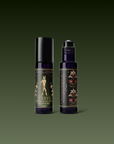 Two dark glass roller bottles of essential oil perfume from the Monthly Magic Tea Journey Subscription stand on a green gradient background: one features a golden goddess with florals, celebrating tea rituals; the other displays ornate botanical designs.