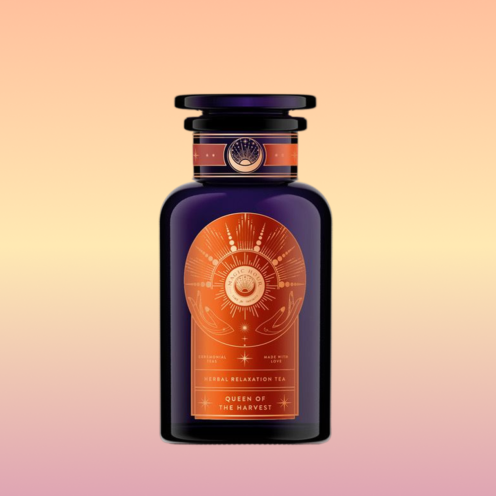 A dark purple glass bottle with an ornate orange celestial label reads "Queen of the Harvest: Herbal Relaxation Tea" and "Caffeine-Free Ashwagandha," set against a peach-to-yellow gradient background.