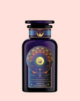 A dark purple bottle with gold and celestial designs, labeled “Queen of the Rainforest: Cacao-Berry Tea,” captures the vibrant spirit of Ecuador’s rainforest, set against a pale pink background.