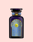 A dark blue bottle with a gold and blue celestial design labeled "Queen of Ukraine: Spring Blossom Tea" stands out on a pastel pink background—ideal for fans of butterfly pea flower or wild strawberry chamomile tea.