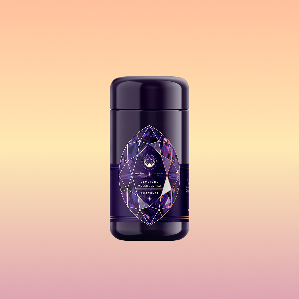 A dark purple tea canister with a geometric amethyst design label stands against a peach-to-yellow background. The label reads “Amethyst: Strawberry-Passionfruit Gemstone Wellness Tea”—herbal tea for clarity and balance.