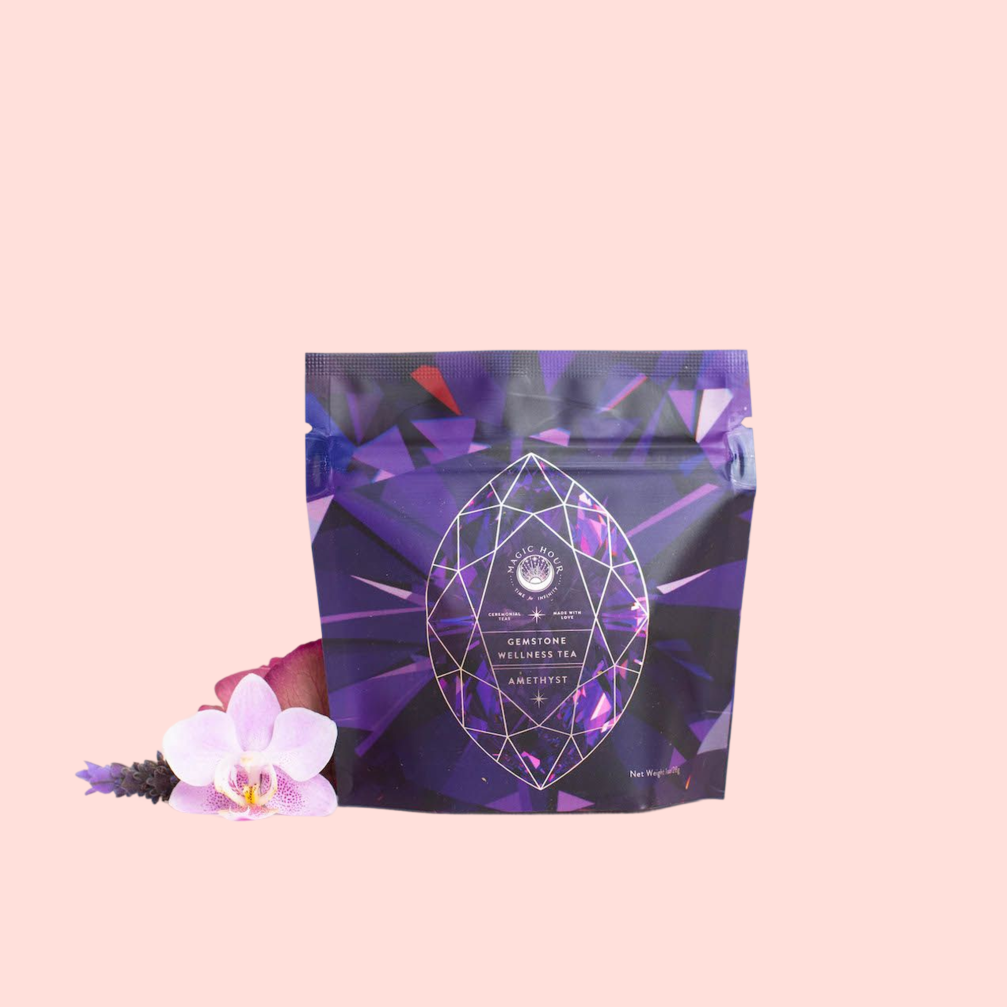 A purple pouch labeled "Amethyst: Strawberry-Passionfruit Gemstone Wellness Tea" stands upright by a pink orchid and lavender sprig, showcasing its organic herbal blend against a pale pink background.