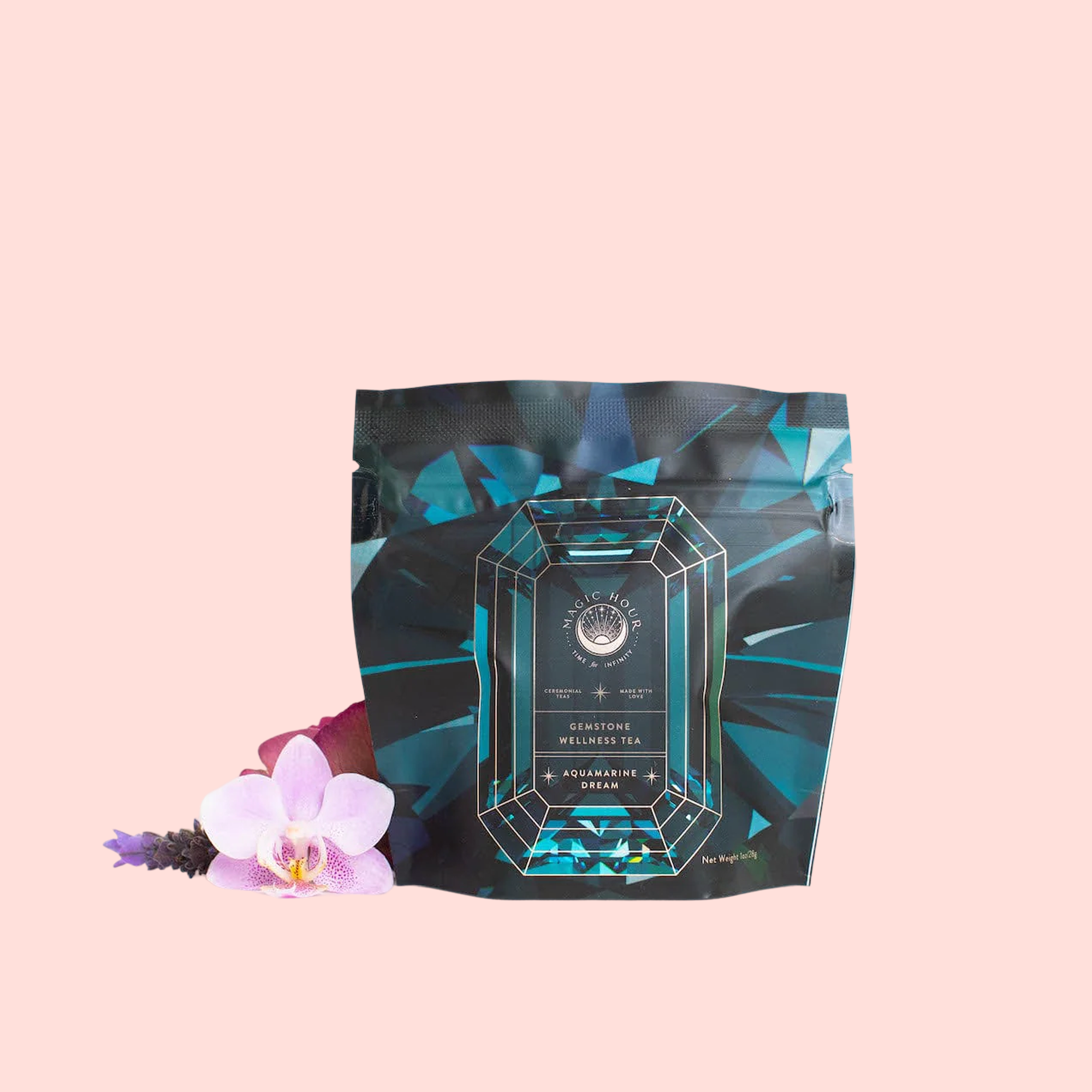 A black and teal geometric tea package labeled "Aquamarine Dream - Soothing Herbal Ayurvedic Adrenal Tonic" rests on a pale pink background, accented by a pink orchid and sprigs of lavender.