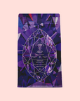 A purple geometric package labeled "Amethyst: Strawberry-Passionfruit Gemstone Wellness Tea" with a crystal-inspired design promotes spiritual wellness and an organic herbal blend against a light pink background.