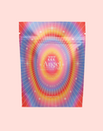 A vibrant tea package labeled "Angel Aid Flower Teas" features "777: Celestial Messengers Dawn Pineapple Passionfruit Green Tea" with radiating lines and starburst designs on a soft pink background.