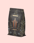 A decorative coffee bag featuring "The Emperor: Green Chaga Chai with Lion's Mane and Reishi," with a robed figure, stars, and floral motifs—perfect for mushroom tea lovers seeking immune support blends.