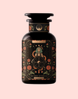 A dark glass bottle labeled "The Wheel of Fortune: Ginseng Spice Tea for Adapting to Change" features ornate floral designs, a mystical sphinx and wheel, and celestial accents on a pale pink background—suggesting a caffeine-free wellness tea.
