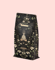 A decorative tea bag labeled "Magic Hour" and "The Oracle: Lemon Lavender Tea for Supporting the Gut-Brain Axis" features floral patterns and a meditating figure, set against a pale pink background for mindful moments.