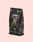A decorative tea bag with a celestial woman, stars, and florals on pastel pink. The label reads "Magic Hour" and "The Star," featuring The Star: Vanilla-Ginger Beauty Potion with Jasmine & Shatavari, an organic herbal blend.