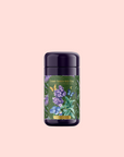 A dark purple tea canister with a colorful floral and blueberry label on a pale pink background. "Blueberry Lavender Mint: Cosmic Garden Iced Tea" by Magic Hour is an antioxidant-rich iced tea blend.