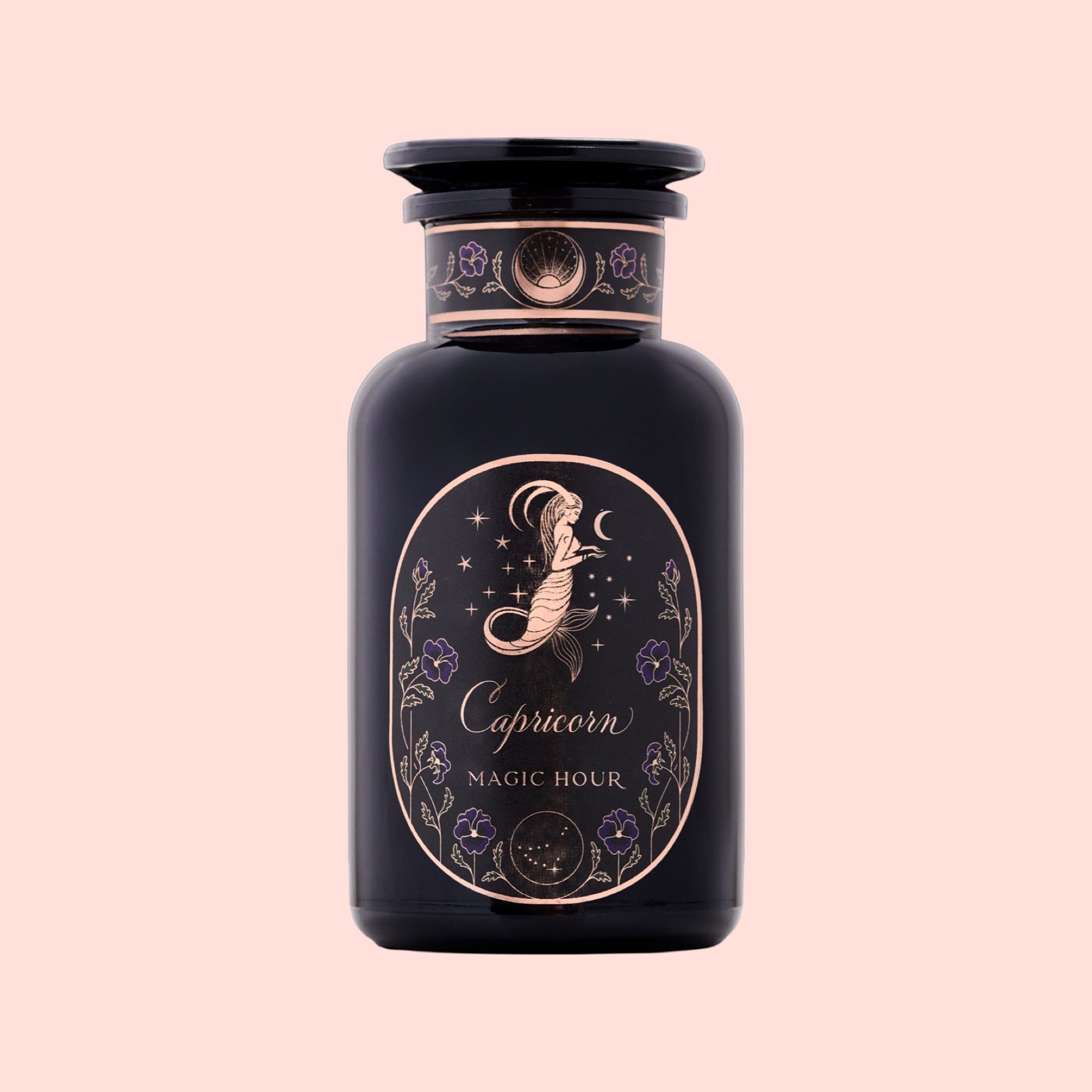 A dark purple glass jar labeled "Capricorn: Maple Oolong Tea" with a gold mermaid, stars, and flower design hints at oolong magic—set against a pale pink background.
