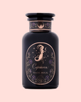 A dark purple glass jar labeled "Capricorn: Maple Oolong Tea" with a gold mermaid, stars, and flower design hints at oolong magic—set against a pale pink background.