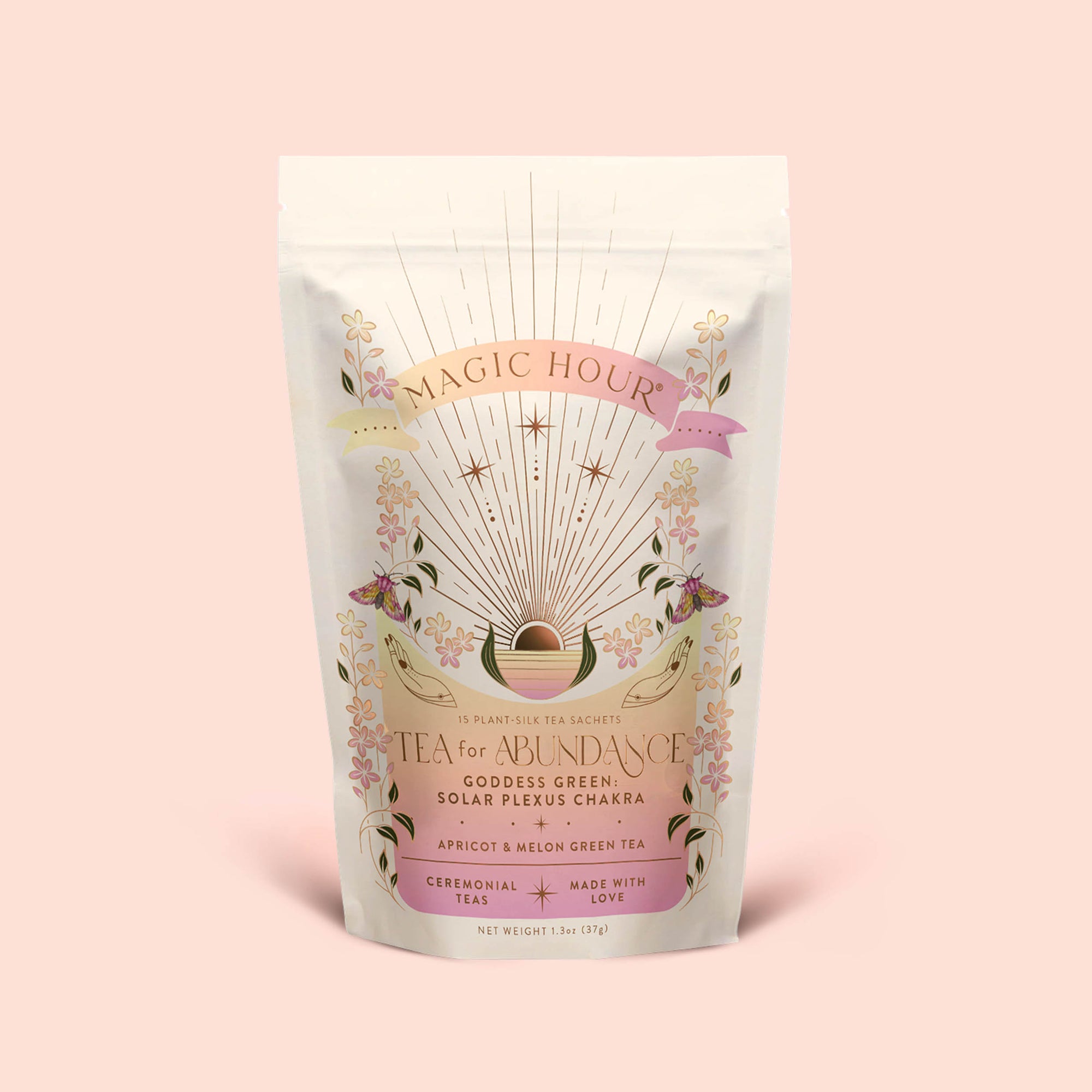 A pastel pouch of Tea for Abundance: Goddess Green: Apricot &amp; Lychee Green Tea features floral designs, gold rays, and text describing it as a solar plexus chakra tea, blending apricot and lychee green tea with organic lemongrass for a biodynamic infusion.