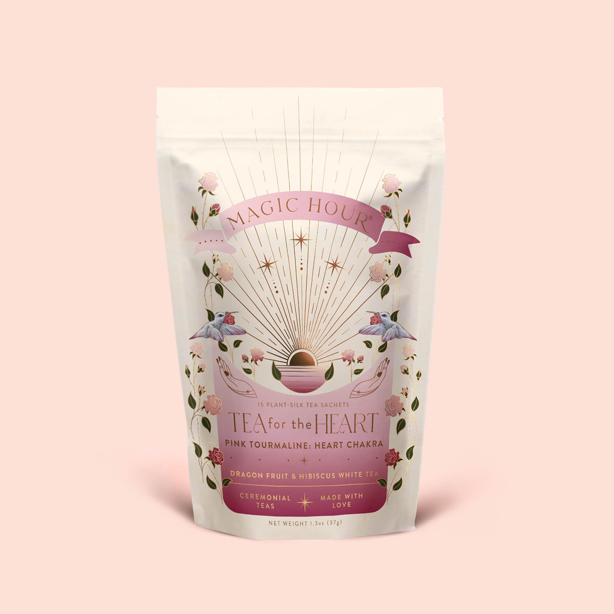 A pastel pouch labeled "Tea for the Heart: Pink Tourmaline: Dragonfruit &amp; Hibiscus White Tea" displays golden rays, pink flowers, and hummingbirds. The text emphasizes adaptogenic herbs alongside dragonfruit and hibiscus white tea, pink tourmaline essence, and ceremonial tea—all presented on a soft pink background.