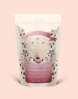 A pastel pouch labeled "Tea for the Heart: Pink Tourmaline: Dragonfruit & Hibiscus White Tea" displays golden rays, pink flowers, and hummingbirds. The text emphasizes adaptogenic herbs alongside dragonfruit and hibiscus white tea, pink tourmaline essence, and ceremonial tea—all presented on a soft pink background.