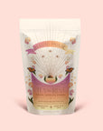 A pastel pouch of Magic Hour’s “Tea for Rest: Venus: Mango Blossom & Nervines Herbal Tea,” adorned with floral and butterfly designs, a celestial motif, and gold accents on a light pink background. This herbal blend features organic chamomile to support relaxation, is labeled as ceremonial, and marked “made with love.”.