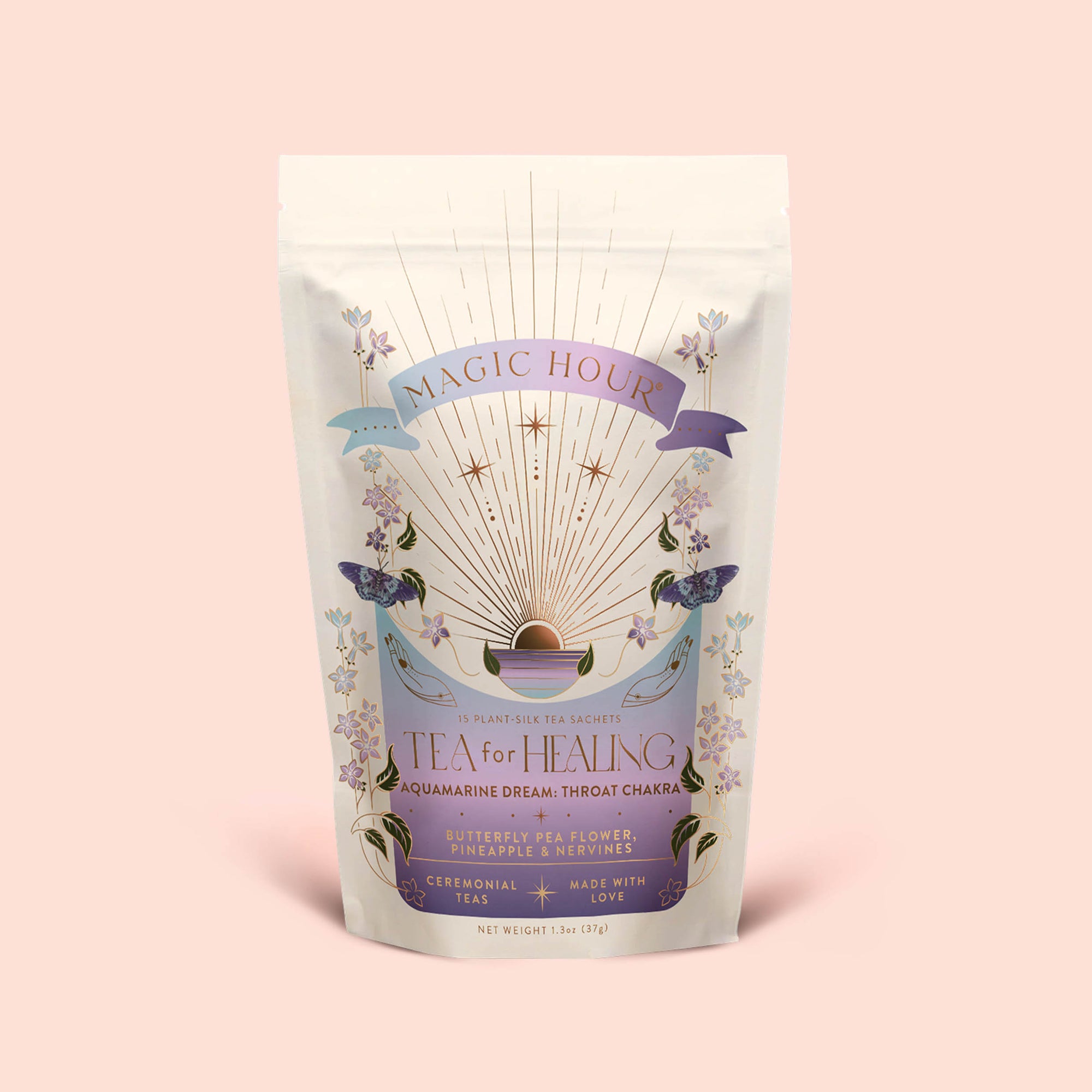 A pastel-colored Magic Hour tea package adorned with floral illustrations, butterflies, and a sunburst design. The label reads "Tea for Healing: Aquamarine Dream: Blueberries, Pineapple &amp; Nervines Herbal Tea," highlighting details like "Butterfly Pea Flower" and "13 sachets." This adaptogenic tea blend is thoughtfully crafted to support restful sleep and gentle nervous system balance, making each cup a soothing ritual.