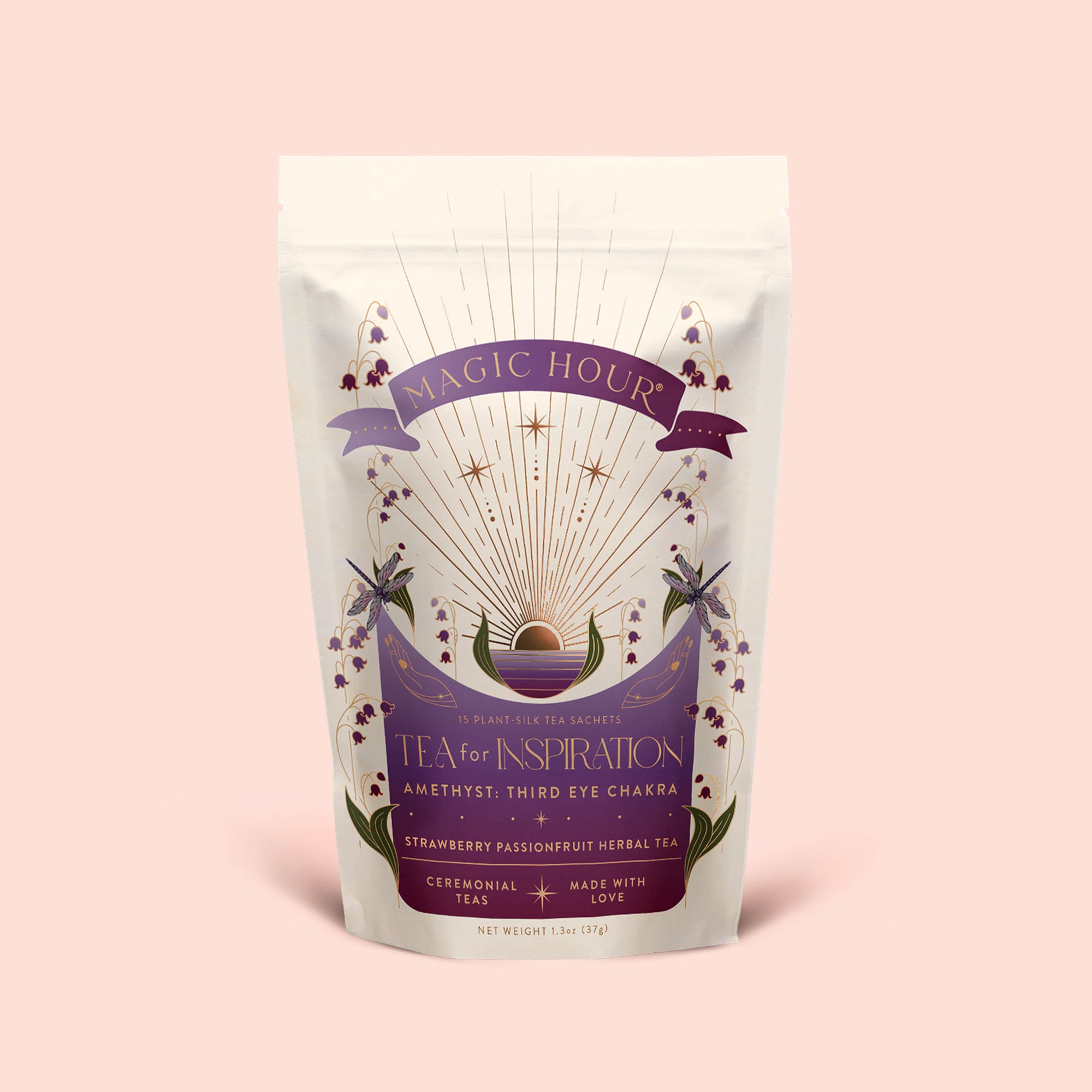 A white pouch of Magic Hour’s “Tea for Inspiration: Amethyst: Strawberry Passion Fruit Herbal Tea Blend,” adorned with a purple sunburst, crystals, and flowers, is specially labeled for the third eye chakra. Crafted to enhance spiritual clarity, this organic herbal blend invites you to awaken your senses and elevate your daily ritual.