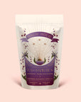 A white pouch of Magic Hour’s “Tea for Inspiration: Amethyst: Strawberry Passion Fruit Herbal Tea Blend,” adorned with a purple sunburst, crystals, and flowers, is specially labeled for the third eye chakra. Crafted to enhance spiritual clarity, this organic herbal blend invites you to awaken your senses and elevate your daily ritual.