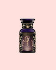 A dark purple perfume bottle with ornate gold floral designs and a fairy illustration on the label, inspired by the ethereal scent of Flora In Bloom: Peach Moonlight White Tea (Yue Guang Bai), set against a light pink background.
