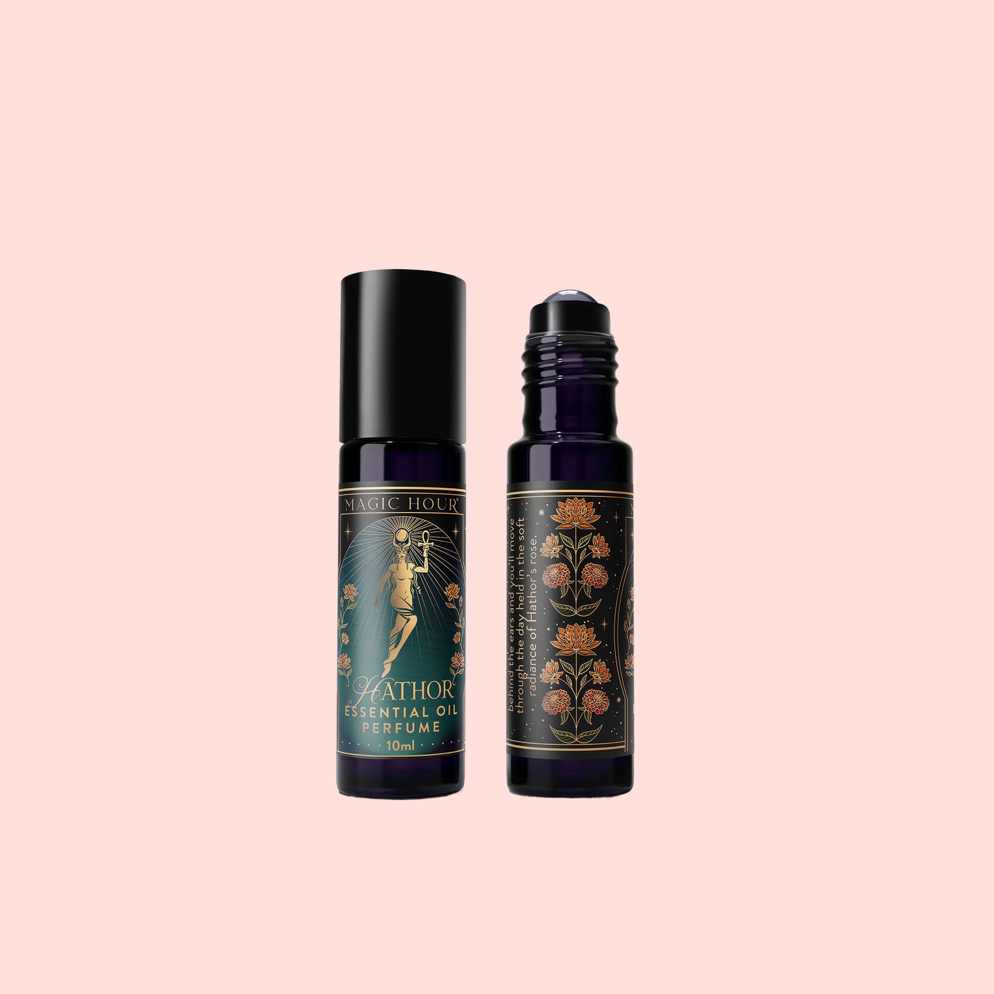 Two dark glass bottles of Hathor of Joy: Essential Oil Perfume, infused with rose essential oil, display vintage-style floral and figure labels. Arranged upright on a light pink background, one features a black cap while the other is topped with a rollerball.