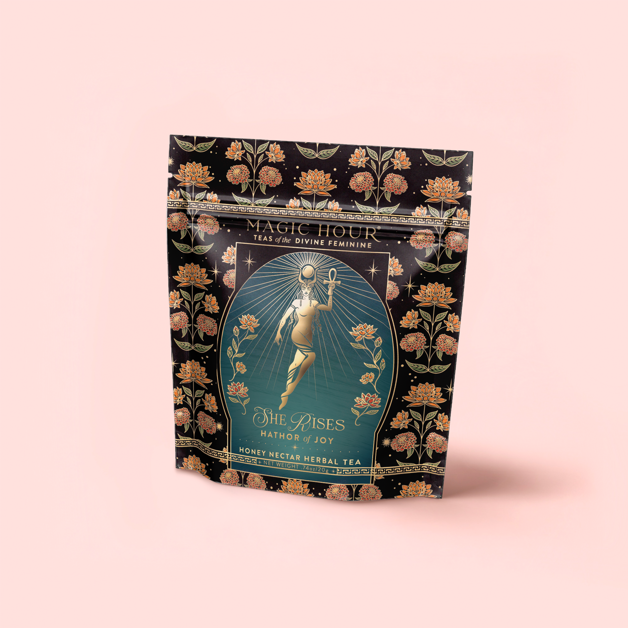 A decorative black tea pouch labeled "Hathor of Joy: Honey Nectar Herbal Tea," featuring an ornate design of a woman with flowers and the text "She Rises—Blue Lotus Honey Nectar Herbal Tea," a caffeine-free blend.
