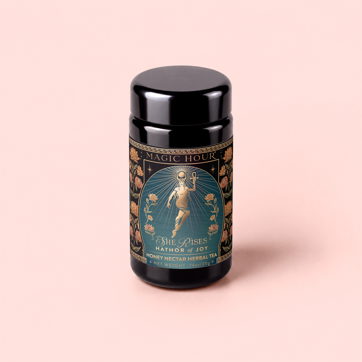 A black tea canister labeled “Magic Hour” features an ornate design with an illustrated woman holding a sun and surrounded by flowers. This caffeine-free blend, called “Hathor of Joy: Honey Nectar Herbal Tea,” is enriched with blue lotus for a soothing herbal tea experience.