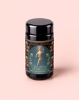 A black tea canister labeled “Magic Hour” features an ornate design with an illustrated woman holding a sun and surrounded by flowers. This caffeine-free blend, called “Hathor of Joy: Honey Nectar Herbal Tea,” is enriched with blue lotus for a soothing herbal tea experience.