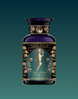 A dark glass bottle from the Monthly Magic Tea Journey Subscription, adorned with gold floral details and a radiant goddess on the label, evokes goddess ritual and herbal wellness against a teal background.