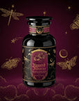 A black apothecary jar labeled “Haunted Hibiscus: Tart Berry Herbal Blend with Warm Spices” stands against a dark purple background adorned with gold illustrations of insects, stars, moons, and clouds—perfect for showcasing this enchanting caffeine-free hibiscus tea blend.