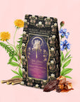 A “Monthly Magic Tea Journey Subscription” box rests among yellow and blue flowers, licorice root, cocoa beans, and caramel chunks, its ornate celestial design evoking a magical goddess tea ritual.