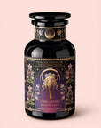 A black tea jar labeled “Monthly Magic Tea Journey Subscription” with floral designs, celestial motifs, and two figures sits against a light pink background.