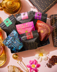 Herbal Tea Sampler Tea Box: Caffeine-Free Teas for Sleep, Digestion & Immunity featuring seven colorful herbal tea pouches, surrounded by a gold teapot, two cups of brewed tea, flowers, and a tea infuser.