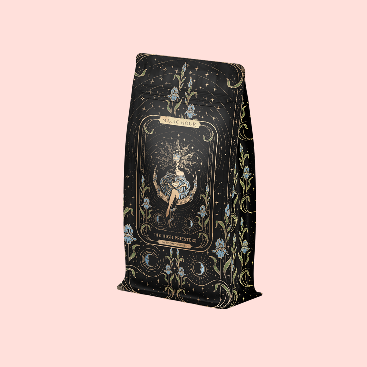 A decorative tea package with an ornate celestial and floral design features a central illustration of a seated woman. The label reads "Magic Hour" and "The High Priestess." This organic, caffeine-free herbal tea comes in a soft pink background. Product: The High Priestess Ginger-Mint-Cardamom Tea Refill Pouch.