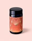 A black canister labeled “Hydrate Tea Boost” in ornate orange and gold rests on a light pink background, inviting you to enjoy this nutrient-rich botanical elixir designed to enhance your daily tea ritual.