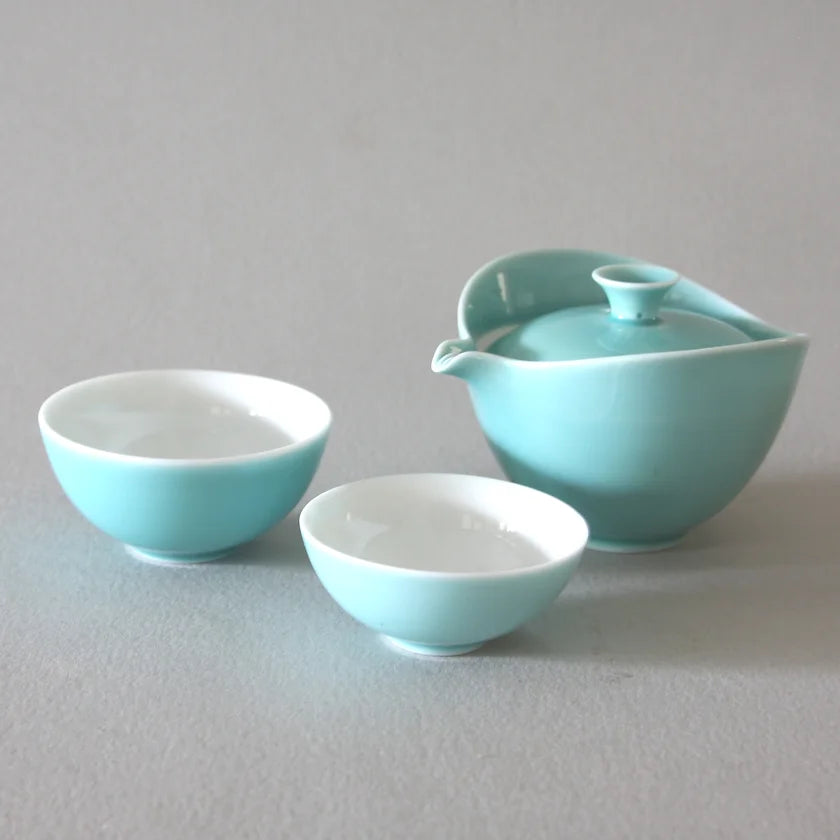 The Ingot Blue Travel Tea Set from Eastern Elm includes a teapot with a lid and two small teacups set against a light gray background. The cups and teapot feature a harmonious color palette, combining soft teal hues with white interiors. The minimalist and elegant design makes it ideal for portable enjoyment.