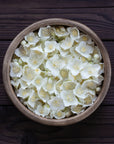 A wooden bowl brimming with delicate magnolia oolong jasmine flowers rests on a dark wooden surface. The white petals create a striking contrast against the rustic background, evoking the sophisticated elegance celebrated by Magic Hour's Triple Moon Tea by Alanis Morissette for her Triple Moon Tour.