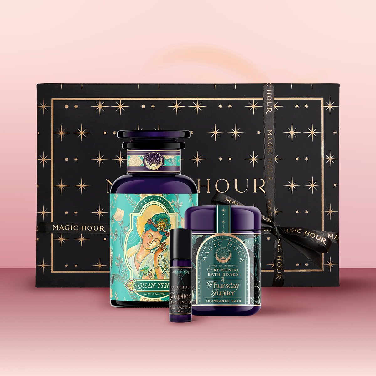 The Jupiter Bath & Beauty Box features three luxury wellness products—one large bottle, one small bottle, and one jar—displayed in front of a black, starry box with gold accents and a “Magic Hour” ribbon for a celestial self-care experience.