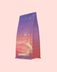 A purple and pink bag of Kapha: Caffeine-Free Saffron Spice Tea features a geometric pattern, starry sky, and person stretching. The label reads "Ayurvedic Infusion, KAPHA, THE EVENING." Supports Ayurvedic digestion without caffeine.