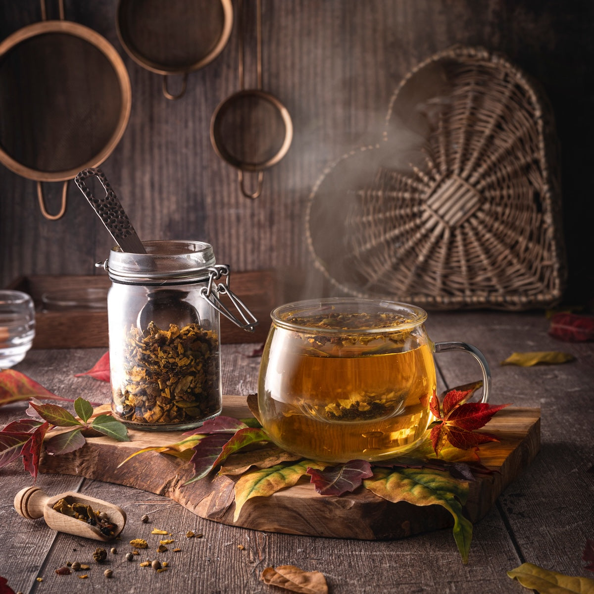 A steaming glass mug of Kettle Corn Kiss—a sweet & nutty toasted rice green tea with caramel & vanilla—rests on a wooden board by autumn leaves and a jar of loose tea, with rustic kitchen decor in the background.