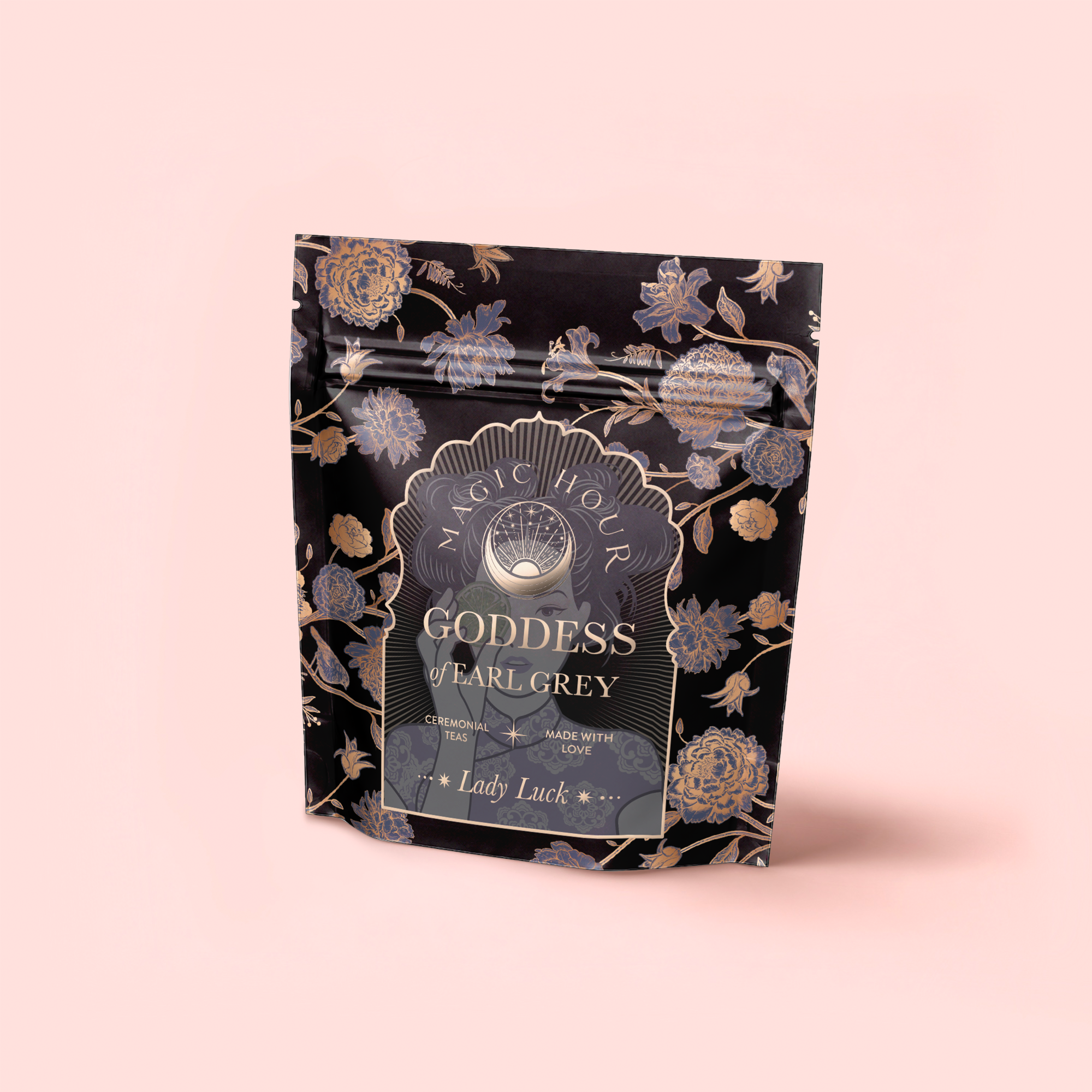 A black and gold floral package labeled "Goddess of Earl: Lady Luck Oriental Beauty Oolong Tea" stands against a light pink background. The label highlights its organic loose leaf Oolong with bergamot essence, made with love.