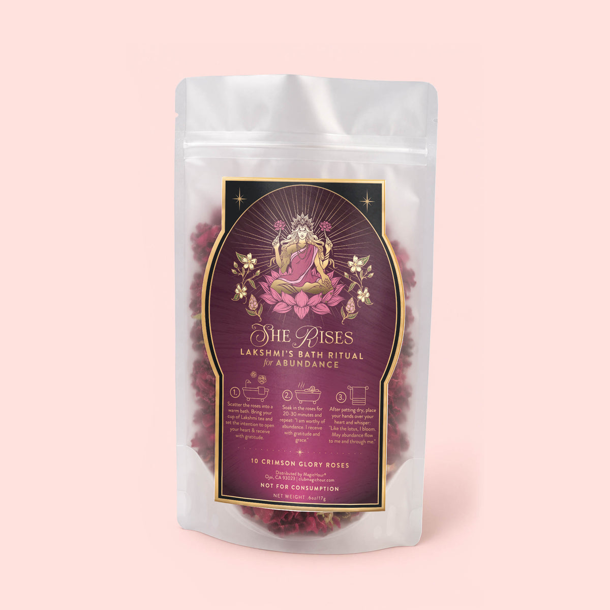 A resealable bag labeled “Lakshmi’s Bath Ritual: Rose Petals for Abundance &amp; Receiving – 10 Roses,” adorned with a decorative goddess motif and floral designs, contains visible dried Crimson Glory Rose petals. The bag is set against a pale pink background.