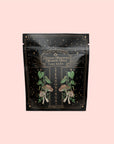 A black and gold resealable pouch labeled "Lapsang Souchong," with illustrated mushrooms, leaves, decorative stars, and "Seasonings" on the front—a smoky black tea seasoning displayed on a pale pink background.