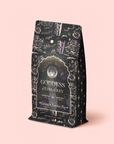 A decorative black tea refill pouch labeled "Lavender London Fog Earl Grey" sits on a light pink background. The packaging features ornate gold and lavender designs with stars and celestial elements, capturing the enchanting essence of Earl Grey tea blended with soothing lavender and bright bergamot notes.