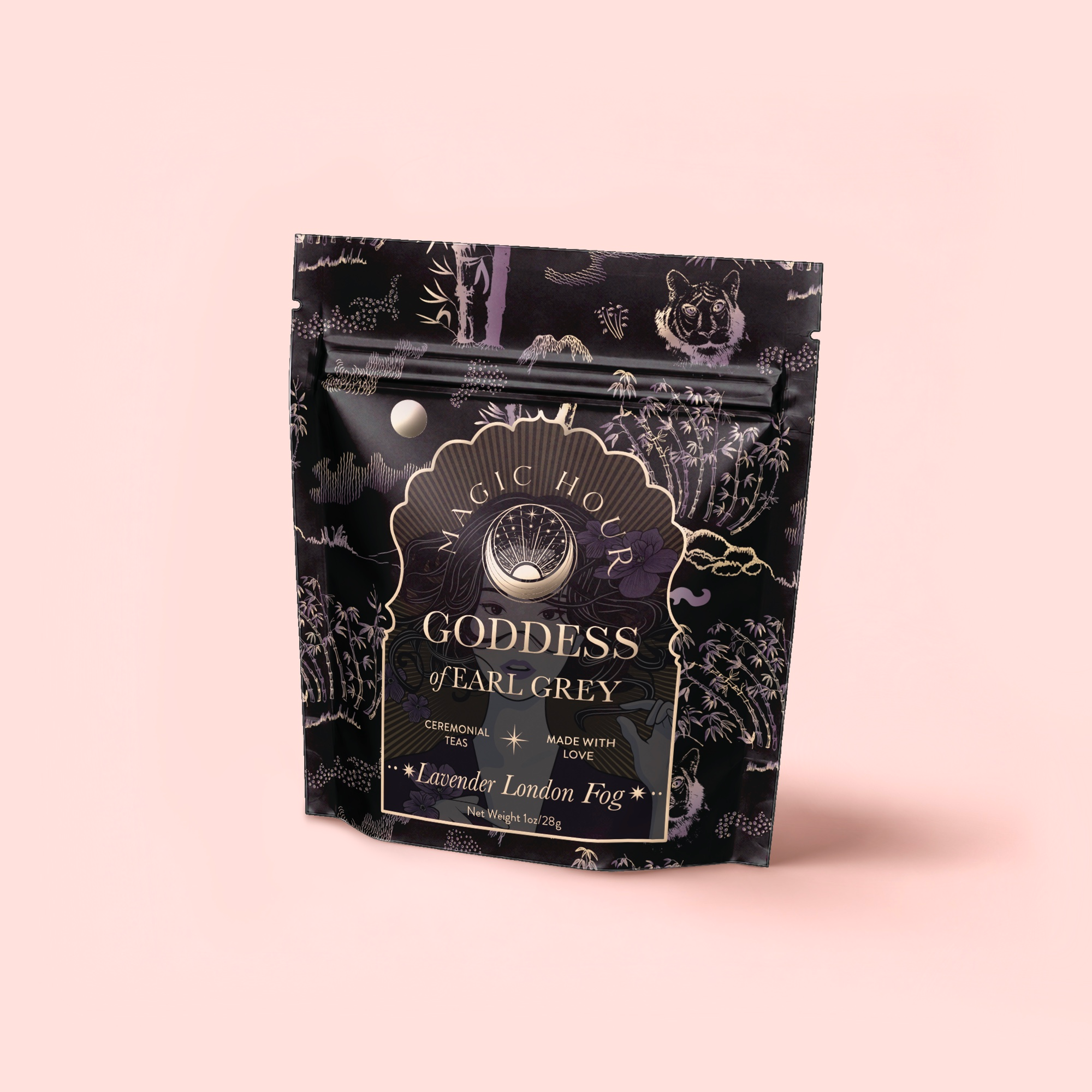 A black and gold pouch of Magic Hour’s Goddess of Earl: Lavender London Fog—Tea for Blooming Clarity & Calm Moods stands upright on a pale pink backdrop, featuring botanical illustrations and labeled as ceremonial bergamot lavender tea.