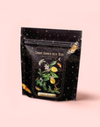 A black resealable pouch of Lemon Meringue Puerh Black Iced Tea by Magic Hour, with a celestial lemon, flower, and butterfly design on light pink—crafted for healthy digestion.