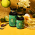 Two bottles of London Fog Oolong tea, with green and gold labels and hints of bergamot, sit amid a clear teacup, lime, roses, spoon, and loose tea. A bright yellow background enhances the vibrant natural theme.