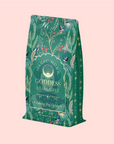 The packaging, featuring colorful birds and botanical illustrations, is for "London Fog Oolong" with a label highlighting hints of bergamot, vanilla, and notes like "Magic Hour Goddess Earl Grey" and "Personal Alchemy." The net weight is 3 oz (100 g).